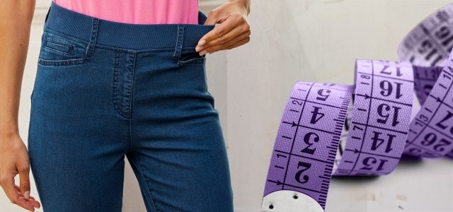 Person trägt blaue Jeans mit elastischem Bund, daneben ein lila Maßband.