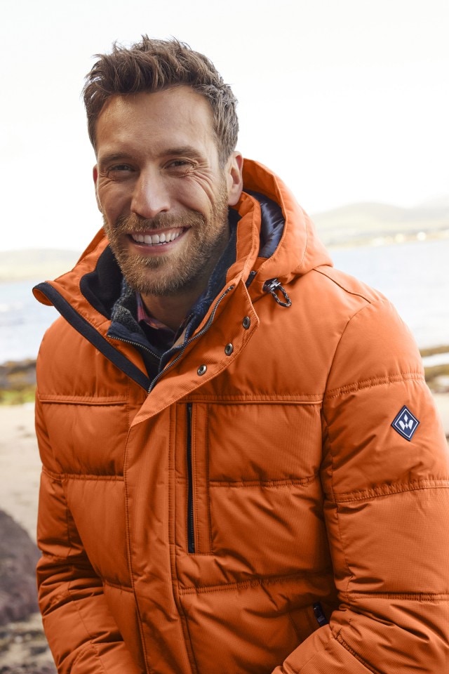 Herr trägt eine orangene Thermo-Jacke und lächelt in die Kamera.