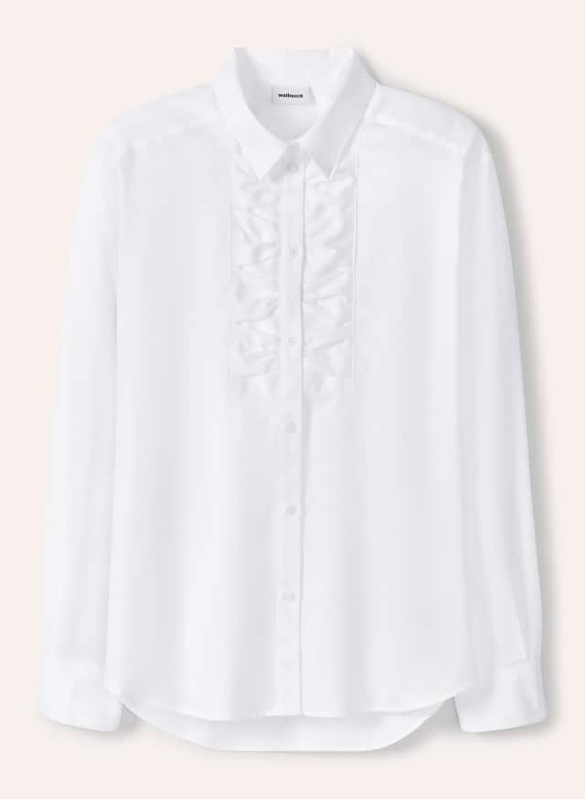 Eine weiße Bluse mit Knopfleiste und dekorativen Rüschen auf der Vorderseite liegt flach ausgebreitet vor hellem Hintergrund.