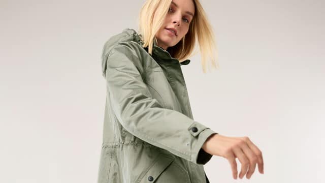 Eine Frau trägt eine hellgrüne Jacke mit Kapuze und bewegt leicht ihren Arm nach vorn.