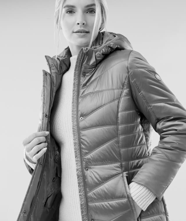 Eine Frau trägt eine gesteppte Winterjacke mit Kapuze und darunter einen grob gestrickten Pullover. Ihr Stil wirkt warm, modern und alltagstauglich.