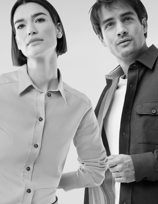 Eine Frau und ein Mann stehen nebeneinander und tragen schlichte, langärmelige Oberteile in einer minimalistisch gehaltenen, schwarz‑weißen Darstellung.