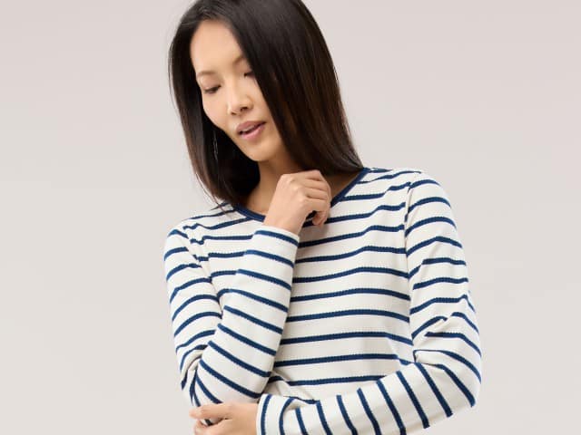 Eine Frau trägt ein weißes Langarmshirt mit dunkelblauen Streifen und blickt nach unten.