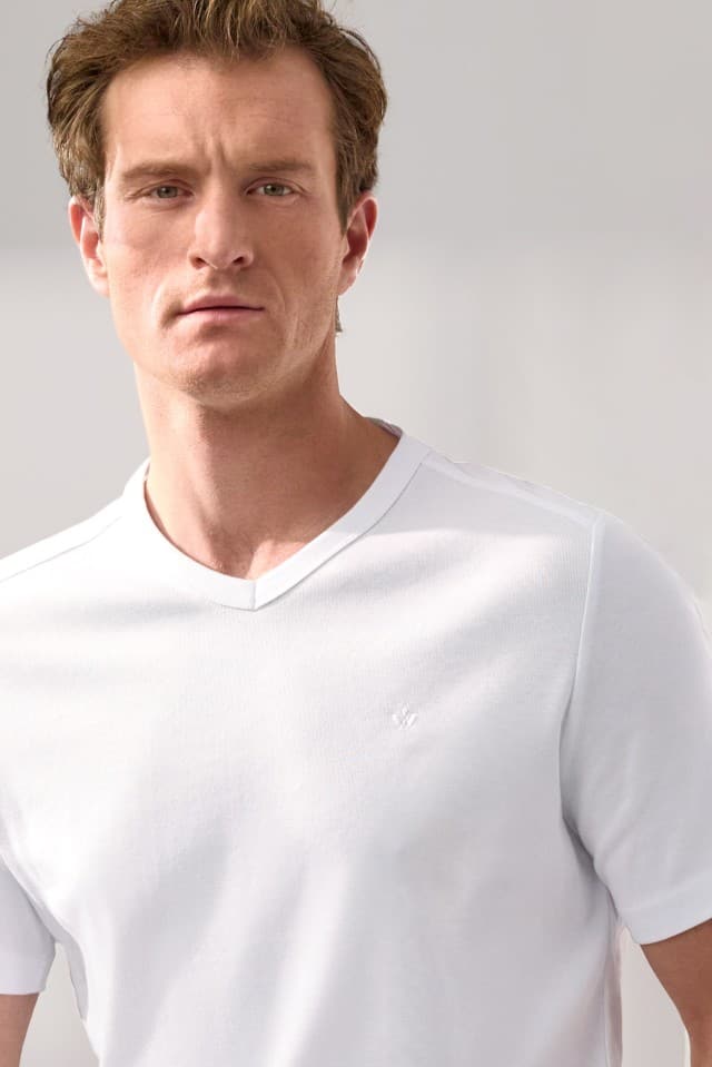 Ein Mann trägt ein weißes T‑Shirt mit V‑Ausschnitt und blickt direkt in die Kamera.
