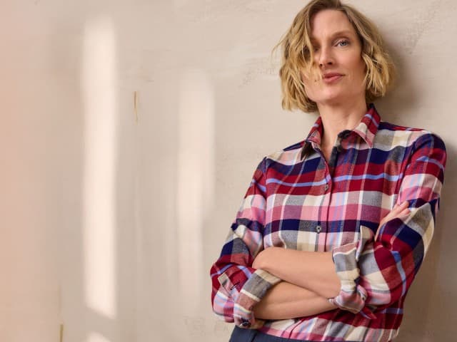 Eine Frau trägt ein kariertes Hemd in Rot-, Blau- und Beigetönen mit aufgerollten Ärmeln. Der lässige Stil wirkt modern und bequem.