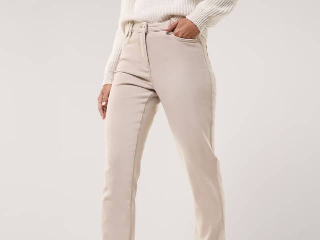Eine Person trägt eine beigefarbene, gerade geschnittene Hose aus festem Stoff. Dazu wird ein cremefarbener Strickpullover kombiniert, was einen schlichten und stilvollen Look ergibt.
