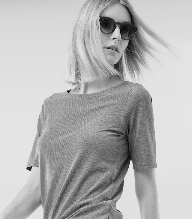 Eine Frau mit Sonnenbrille trägt ein einfarbiges T-Shirt und schaut zur Seite. 