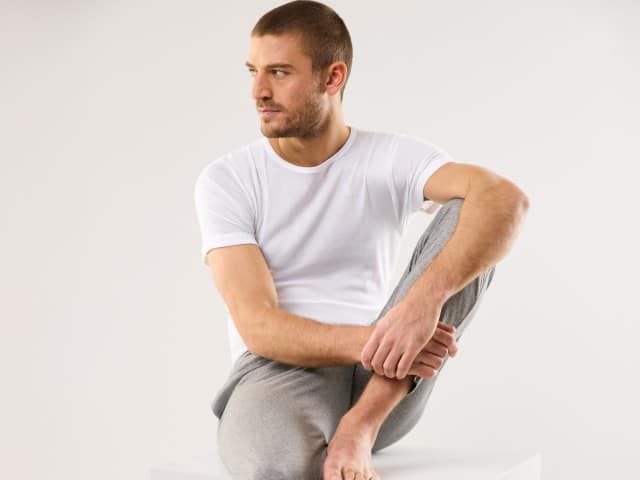 Ein sitzender Mann trägt eine 24/7 Hose in Grau, dazu ein weißes T-Shirt.