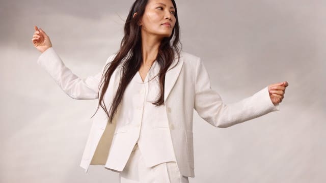 Eine Person trägt einen weißen Anzug mit Jacke, Weste und passender Hose und breitet leicht die Arme aus, während sie zur Seite blickt.