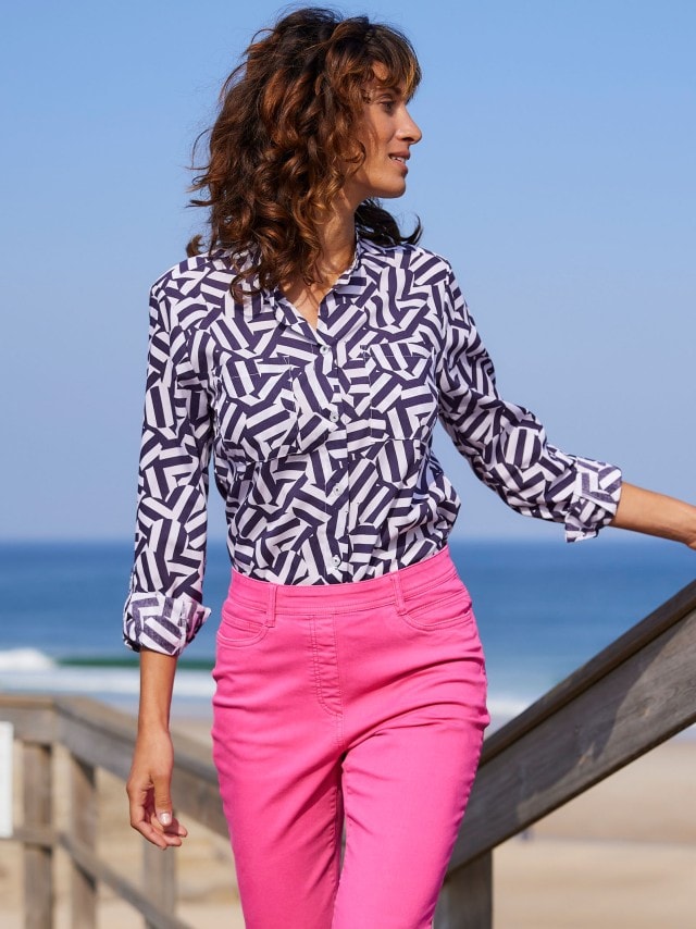 Frau am Strand mit pinker Hose und gemusterter Bluse