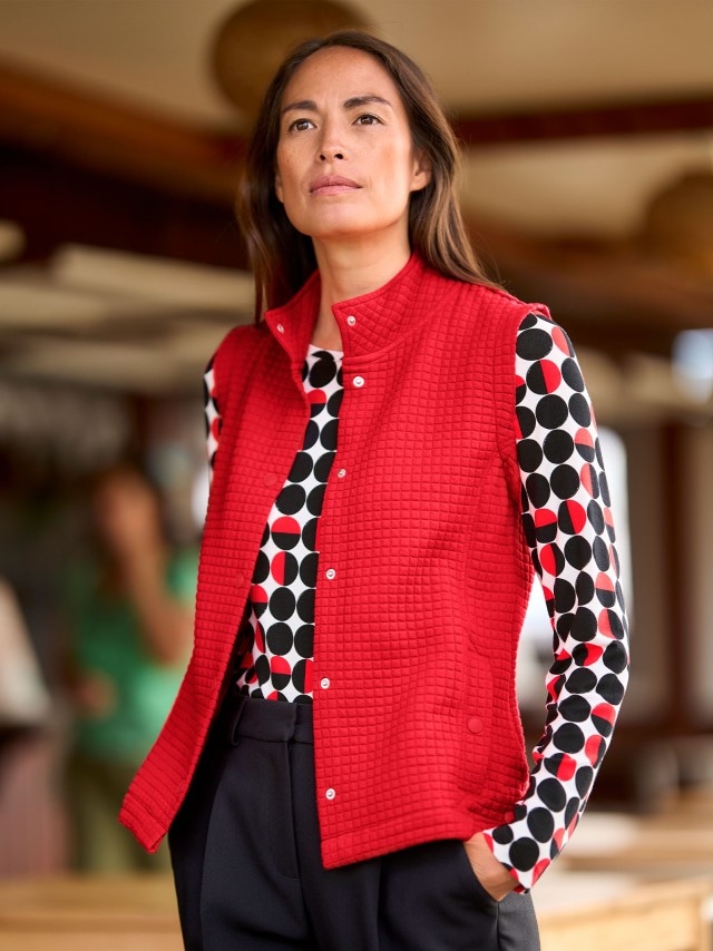 Frau in roter Struktur Jerseyweste und gemustertem Langarm-Shirt.