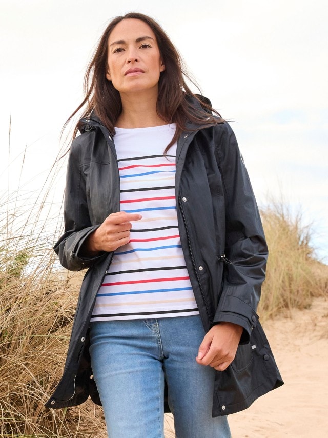 Frau in den Dünen trägt Aquastop Parka Crinkle 2.0, ein gestreiftes Shirt und Jeans
