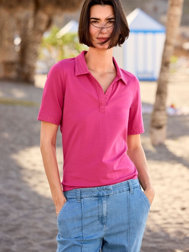 Frau trägt ein Poloshirt Lochstickerei in Pink und hält ihre Hände in den Hosentaschen