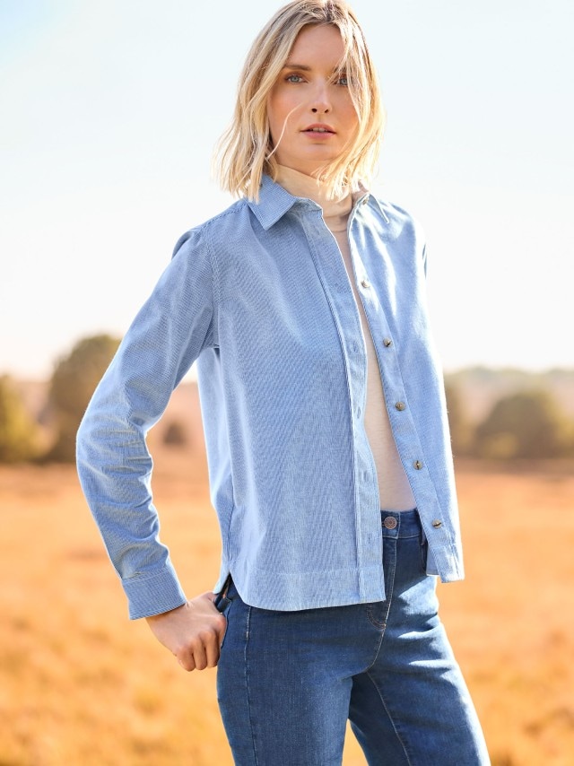 Getragen wird ein hellblaues Hemd über einem beigen Rollkragenpullover und einer Jeans. Der Stil wirkt klassisch, lässig und ideal für den Herbst.