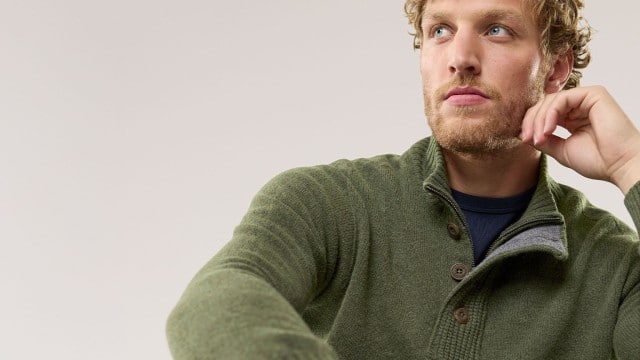 Ein Mann trägt einen olivgrünen Strickpullover mit Knopfleiste und hohem Kragen. Der Stil wirkt gemütlich, natürlich und sportlich-elegant. Ein Mann trägt einen olivgrünen Strickpullover mit Knopfleiste und hohem Kragen. Der Stil wirkt gemütlich, natürlich und sportlich-elegant.
