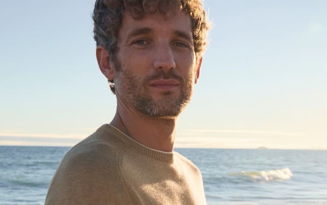 Ein Mann am Strand, trägt einen Pullover in Beige.