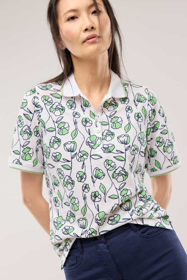 Eine Frau trägt ein Extraglatt Polo mit Blumenmuster in Salbei.