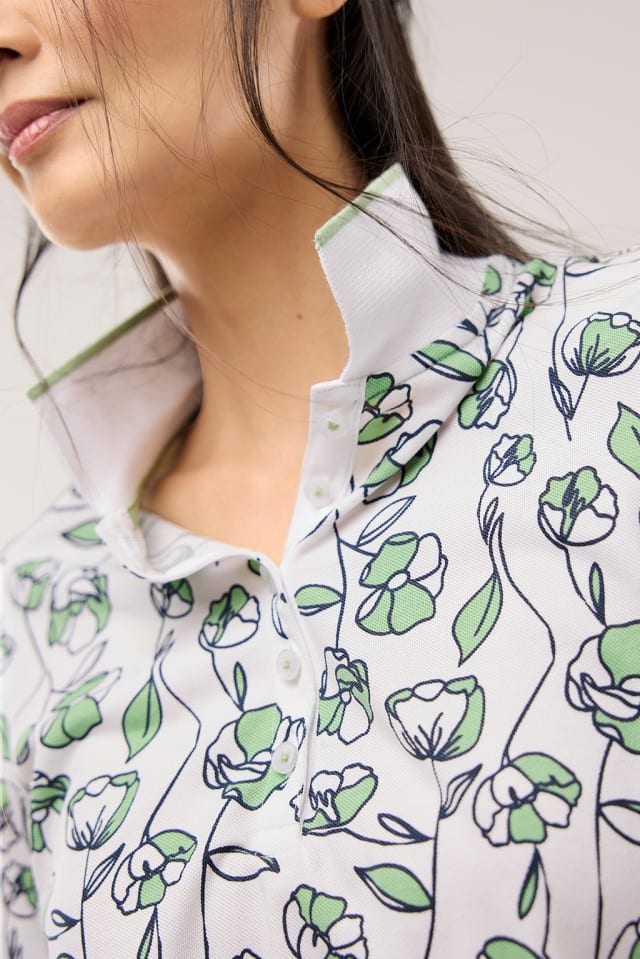 Eine Frau trägt ein Extraglatt Polo mit Blumenmuster in Salbei.