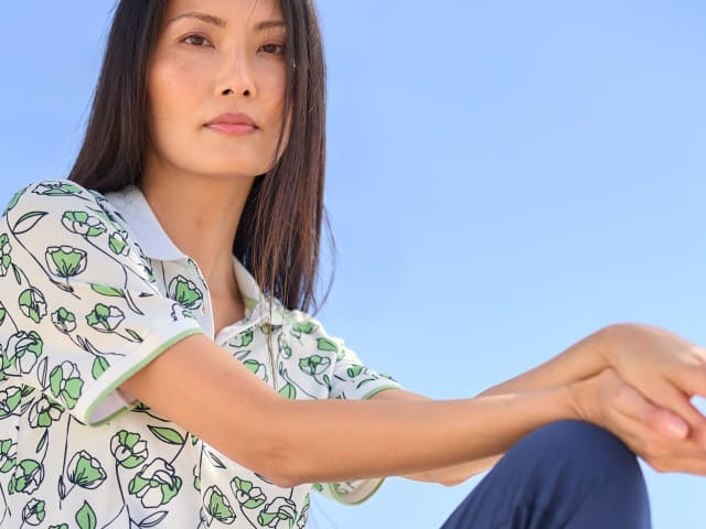 Eine Frau trägt ein Extraglatt Polo mit Blumenmuster in Salbei.