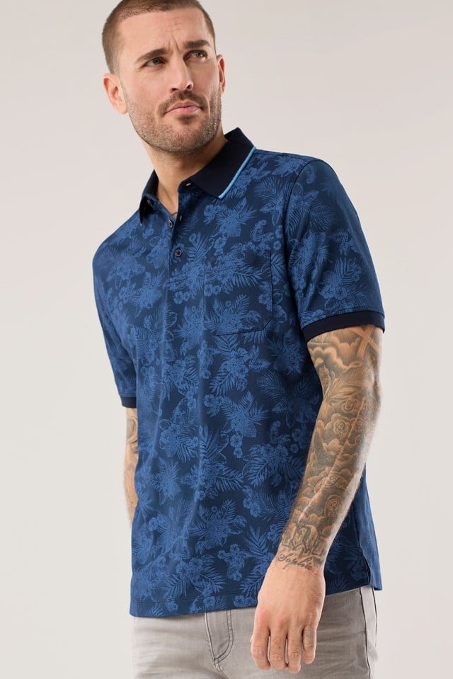 Ein Mann trägt ein blaues Extraglatt-Polo Bicolor mit Blütenmuster.