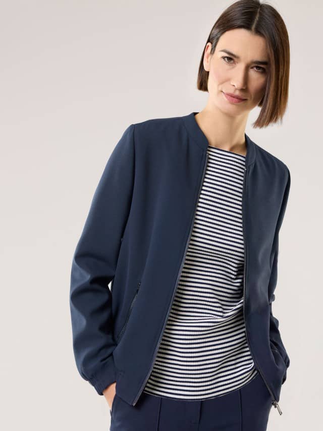 Eine Frau trägt eine dunkelblaue Jacke über einem blau‑weiß gestreiften Oberteil.