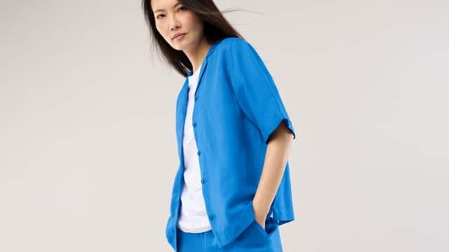 Eine Frau trägt ein leuchtend blaues, locker fallendes Set aus Kurzarmhemd und Hose über einem weißen Oberteil, was einen modernen, frischen und dynamisch‑entspannten Eindruck vermittelt.