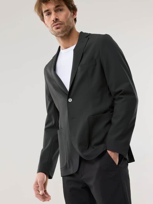 Ein Mann trägt einen schwarzen, modern geschnittenen Anzug über einem weißen T‑Shirt, was klar, minimalistisch und entspannt‑stilvoll wirkt.