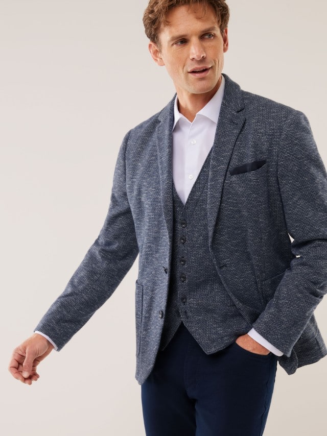 Ein Mann trägt eine blau strukturierte Jacke mit passender Weste zu einem weißen Hemd, was modern, gepflegt und angenehm entspannt wirkt.