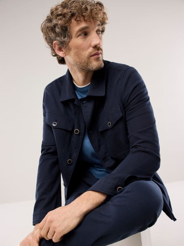 Ein Mann trägt ein dunkelblaues Freizeit‑Set aus Jacke und Hose über einem blauen Shirt, was lässig, modern und ruhig wirkt.
