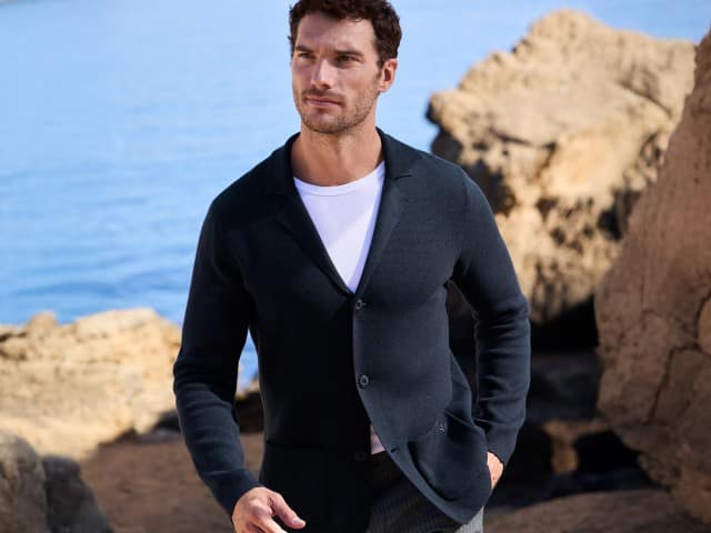 Ein Mann trägt eine dunkelblaue Strickjacke über einem weißen T-Shirt. Sein Stil wirkt lässig, elegant und perfekt für den Frühling.