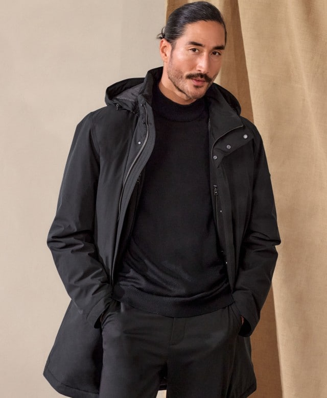 Ein Mann trägt ein komplett schwarzes Outfit mit Hose, Pullover und einer leichten Jacke. Der Look ist schlicht, modern und elegant.