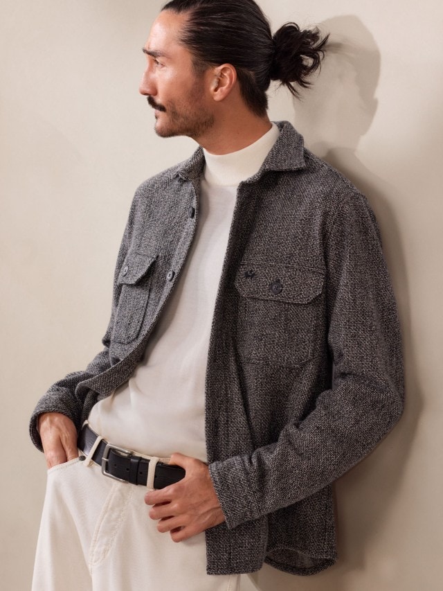 Ein Mann trägt ein weißes Rollkragenshirt mit einer grauen, strukturierten Hemdjacke. Dazu kombiniert er eine helle Hose und einen schwarzen Gürtel für einen modernen, lässigen Look.