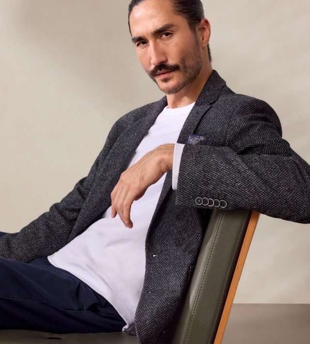 Ein Mann trägt ein weißes T-Shirt mit einem dunklen, gemusterten Sakko. Dazu kombiniert er eine dunkelblaue Hose für einen modernen, smart-lässigen Look.