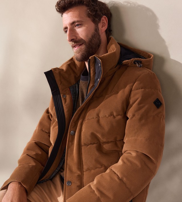 Ein Mann trägt einen braunen Pullover, kombiniert mit einer passenden wattierten Cordjacke. Der Look wirkt herbstlich, lässig und trotzdem stilvoll.