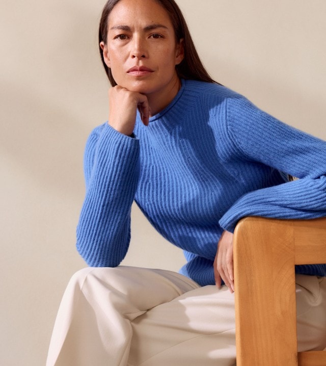 Eine Frau trägt einen gerippten, leuchtend blauen Pullover. Dazu kombiniert sie eine weite, hellbeige Hose für einen frischen und eleganten Look.