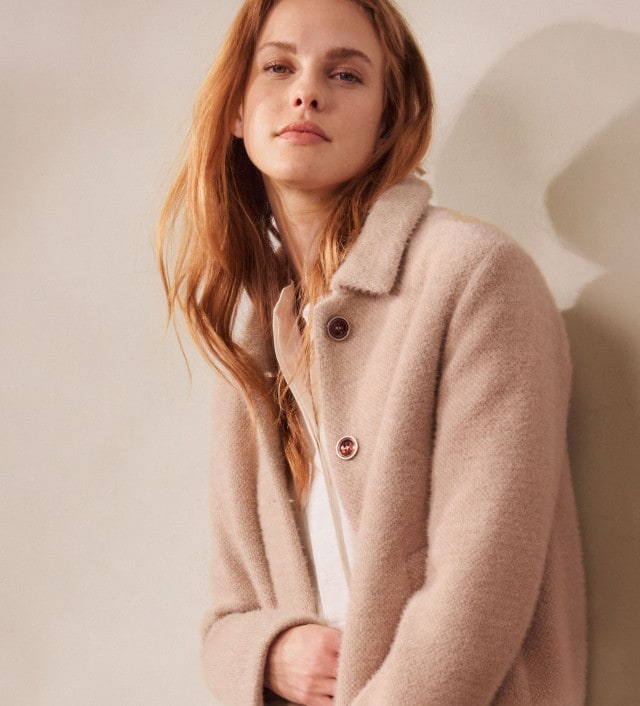 Eine Frau trägt einen beigen Wollmantel mit großen Knöpfen über einem schlichten Oberteil. Der Look ist zeitlos, elegant und dezent modern.