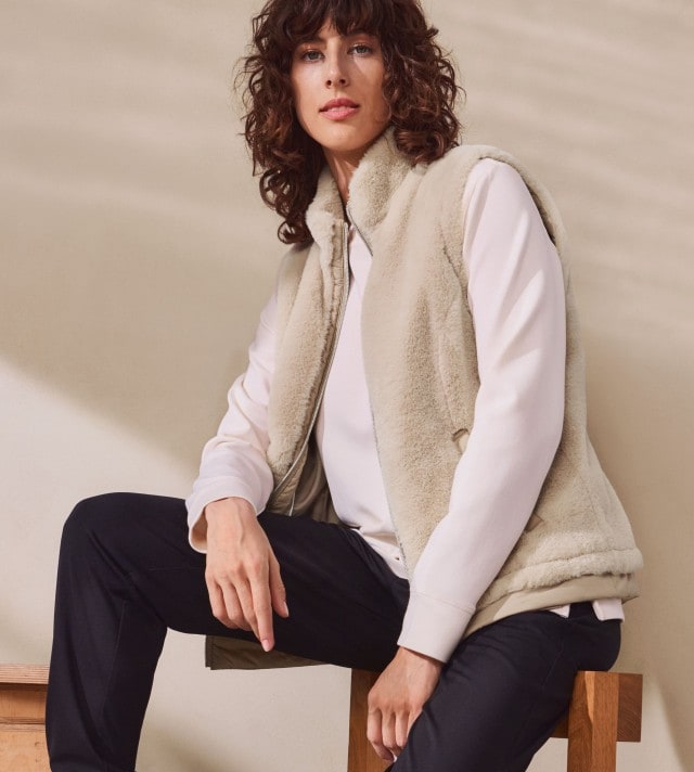 Eine Frau trägt eine helle Fleeceweste über einem weißen Langarmshirt. Dazu kombiniert sie eine schwarze Hose für ein sportlich-gemütliches Outfit.