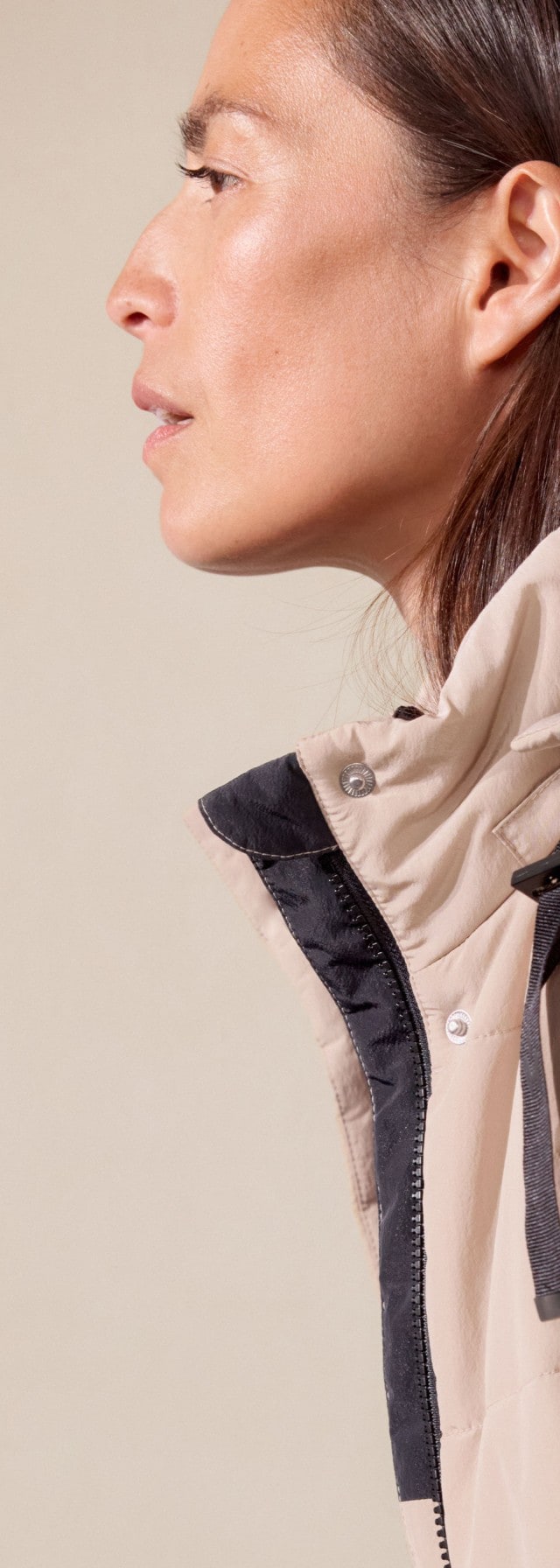 Eine Frau trägt einen beigen Steppmantel mit Kapuze über einem schlichten schwarzen Oberteil. Der Look ist modern, minimalistisch und funktional für kalte Tage.