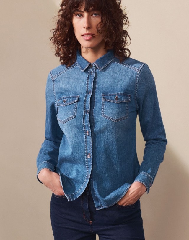 Eine Frau trägt ein klassisches Jeanshemd mit Brusttaschen. Dazu kombiniert sie eine dunkle Jeans für einen zeitlosen Denim-auf-Denim-Look.