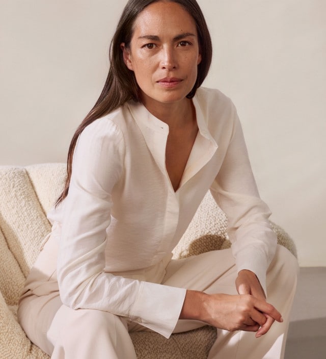 Eine Frau trägt eine schlichte, weiße Bluse, kombiniert mit heller oder dunkler Hose. In einem Look ergänzt sie das Outfit mit einer dunklen Strickjacke für einen klassisch-eleganten Stil.