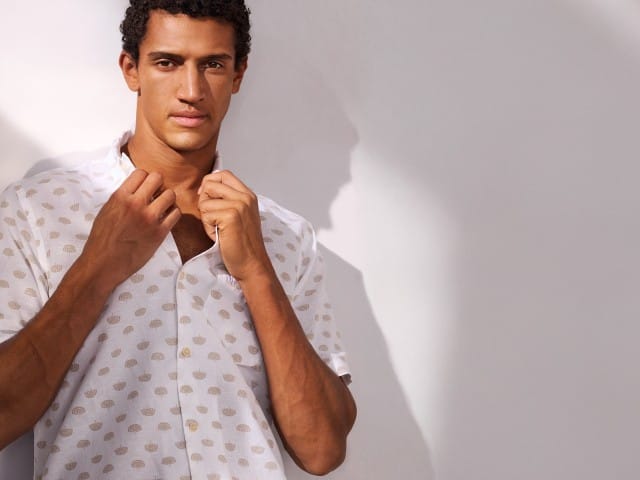 Ein Mann trägt ein Leinen-Mix Revers-Kragen-Hemd und hält den Kragen mit beiden Händen fest. Ein Mann trägt ein Leinen-Mix Revers-Kragen-Hemd und hält den Kragen mit beiden Händen fest.