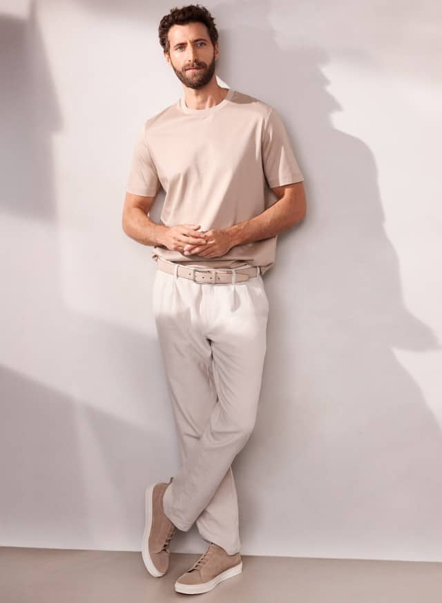Ein Mann an eine Wand gelehnt, trägt ein Premium T-Shirt in der Farbe Sand, dazu eine helle Premium Leinen-Chino. Ein Mann an eine Wand gelehnt, trägt ein Premium T-Shirt in der Farbe Sand, dazu eine helle Premium Leinen-Chino.