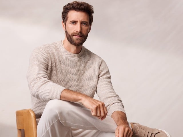 Ein Mann sitzt lässig auf eine Stuhl und trägt einen Mouline Pullover in der Farbe Sand, dazu eine helle Chino. Ein Mann sitzt lässig auf eine Stuhl und trägt einen Mouline Pullover in der Farbe Sand, dazu eine helle Chino.