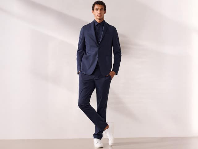 Ein Mann trägt einen Travel Anzug mit Hemd in Marine und weiße Sneaker. Ein Mann trägt einen Travel Anzug mit Hemd in Marine und weiße Sneaker.