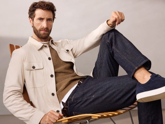 Ein Mann sind entspannt auf einem Sessel und trägt eine Hemdjacke aus Microvelours in Beige, darunter einen Pullover in der Farbe Latte und dazu eine Jeans. Ein Mann sind entspannt auf einem Sessel und trägt eine Hemdjacke aus Microvelours in Beige, darunter einen Pullover in der Farbe Latte und dazu eine Jeans.