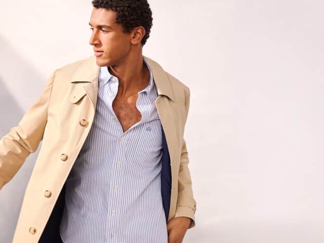 Ein Mann trägt einen Baumwoll Mantel 2 in 1 in Beige, darunter ein Hemd in hellblau. Ein Mann trägt einen Baumwoll Mantel 2 in 1 in Beige, darunter ein Hemd in hellblau.