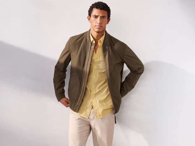 Ein Mann trägt einen Baumwoll Leichtblouson in Oliv, darunter ein Soft-Cotton Hemd in Gelb und dazu eine Ultraleicht Five Pocket in Beige. Ein Mann trägt einen Baumwoll Leichtblouson in Oliv, darunter ein Soft-Cotton Hemd in Gelb und dazu eine Ultraleicht Five Pocket in Beige.