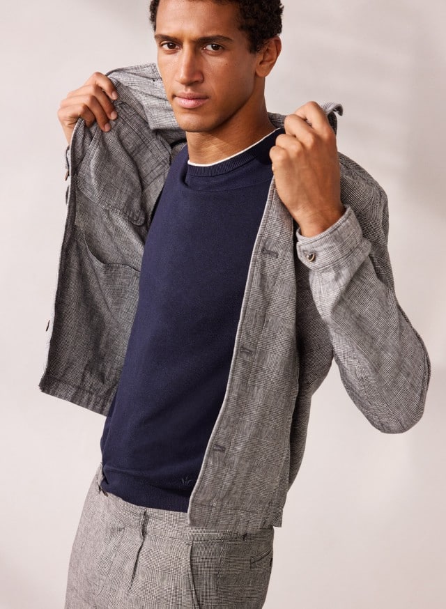 Ein Mann trägt eine Leinen Hemdjacke in Karo Schwarz, darunter ein dunkles Shirt und eine graue Hose. Ein Mann trägt eine Leinen Hemdjacke in Karo Schwarz, darunter ein dunkles Shirt und eine graue Hose.