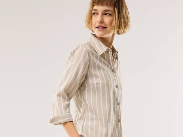 Eine Frau trägt eine gestreifte Leinen-Bluse in Beige.