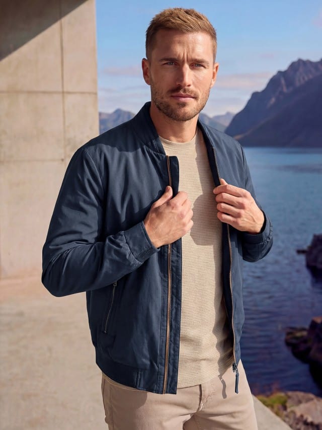 Ein Mann trägt einen Baumwoll Leichtblouson, darunter ein Shirt in der Farbe Sand, dazu die passende Hose.